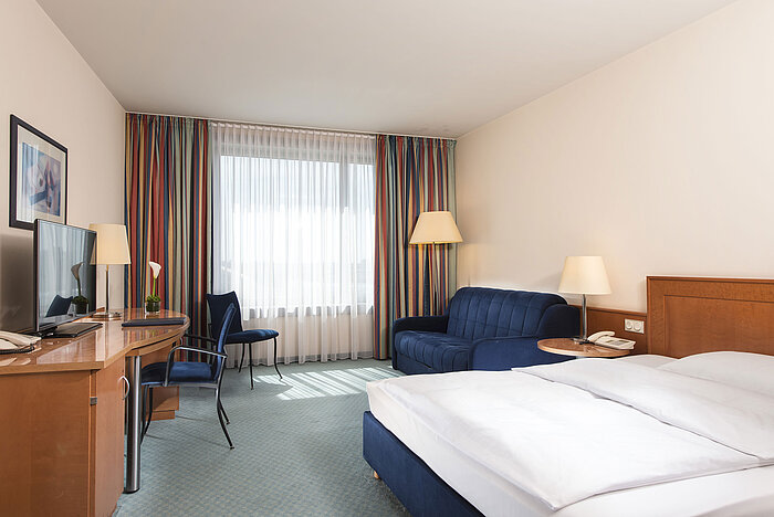 Classic Zimmer im Maritim Hotel Frankfurt mit Doppelbett, Schreibtisch, Sofa und großen Fenstern für viel Tageslicht.