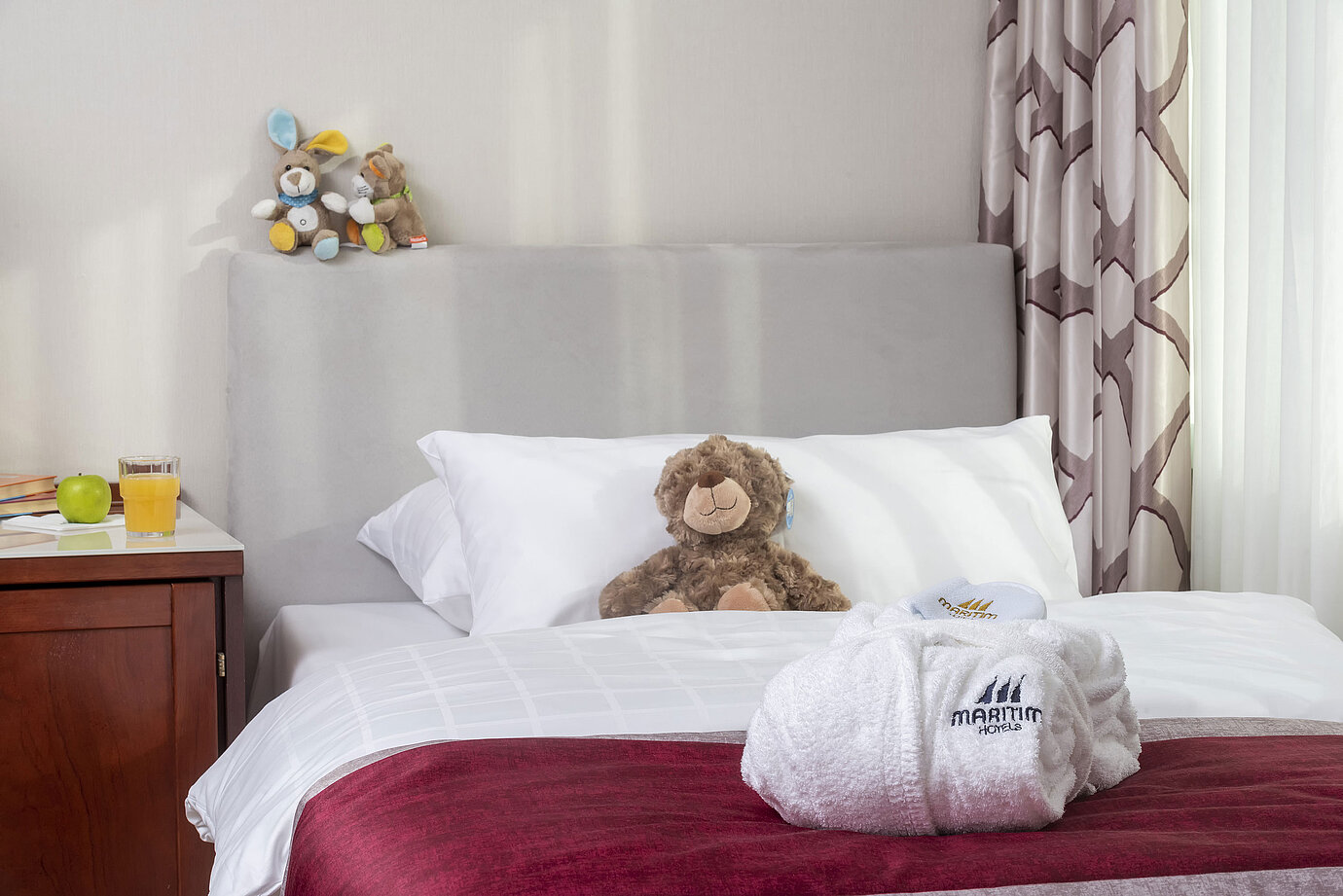 Familiensuite im Maritim Hotel Bonn mit einem gemütlichen Bett, Kuscheltieren und Bademantel, perfekt für Kinder.