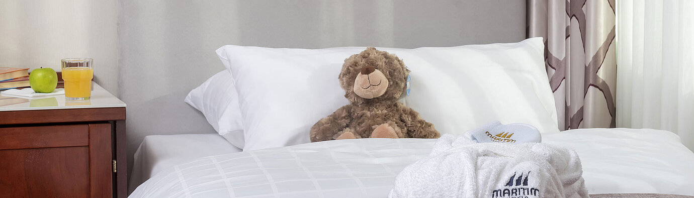 Familiensuite im Maritim Hotel Bonn mit einem gemütlichen Bett, Kuscheltieren und Bademantel, perfekt für Kinder.