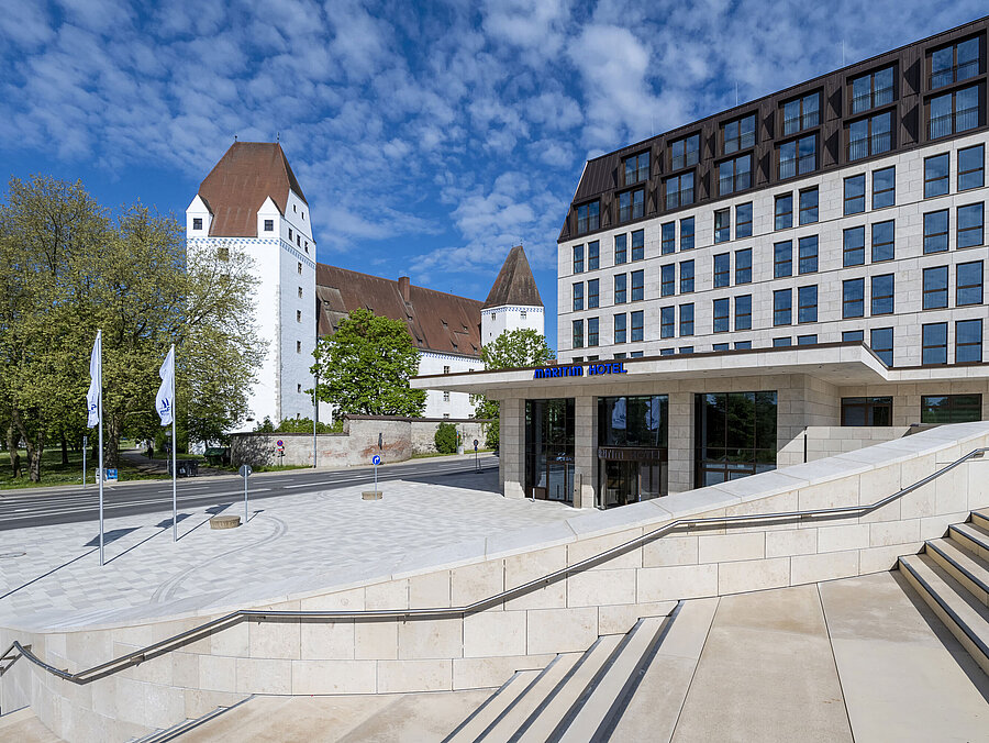 Modernes Maritim Hotel Ingolstadt mit dem historischen Neuen Schloss im Hintergrund und einladendem Eingangsbereich.