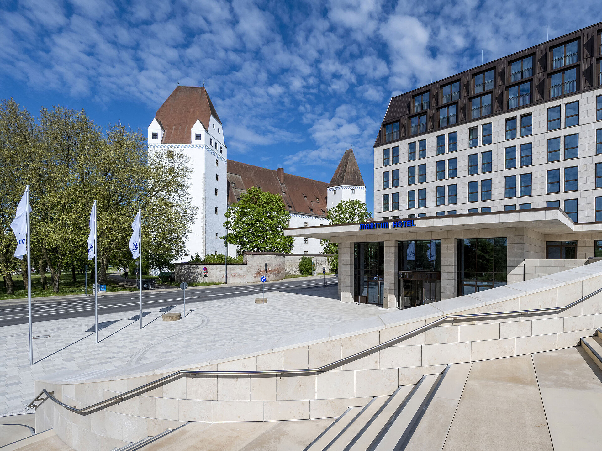 Außenansicht Das moderne Maritim Hotel Ingolstadt mit dem historischen Neuen Schloss im Hintergrund und einladendem Eingangsbereich.