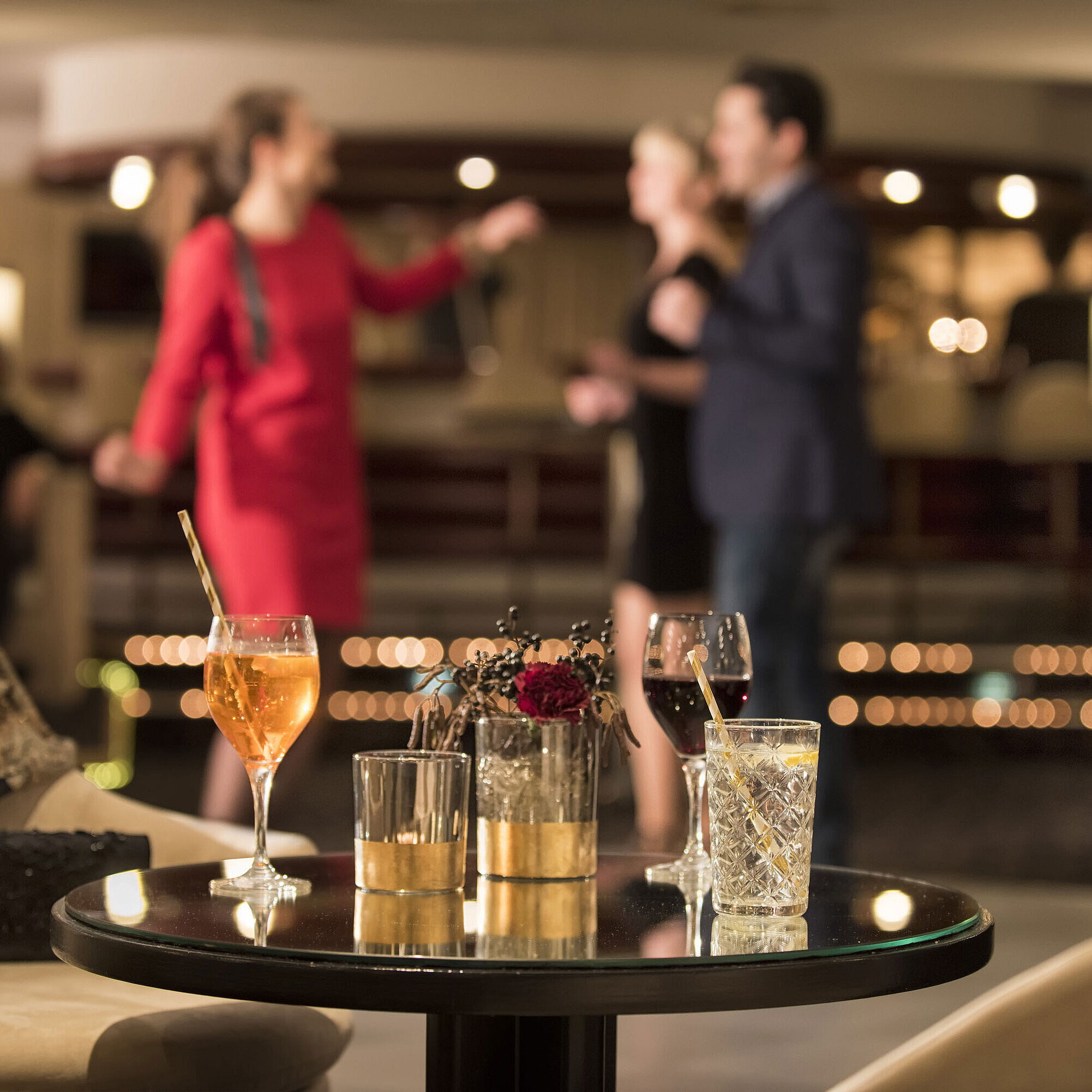 Tisch mit Cocktails und Drinks, während Gäste in der Bar des Maritim Seehotel Timmendorfer Strand tanzen.