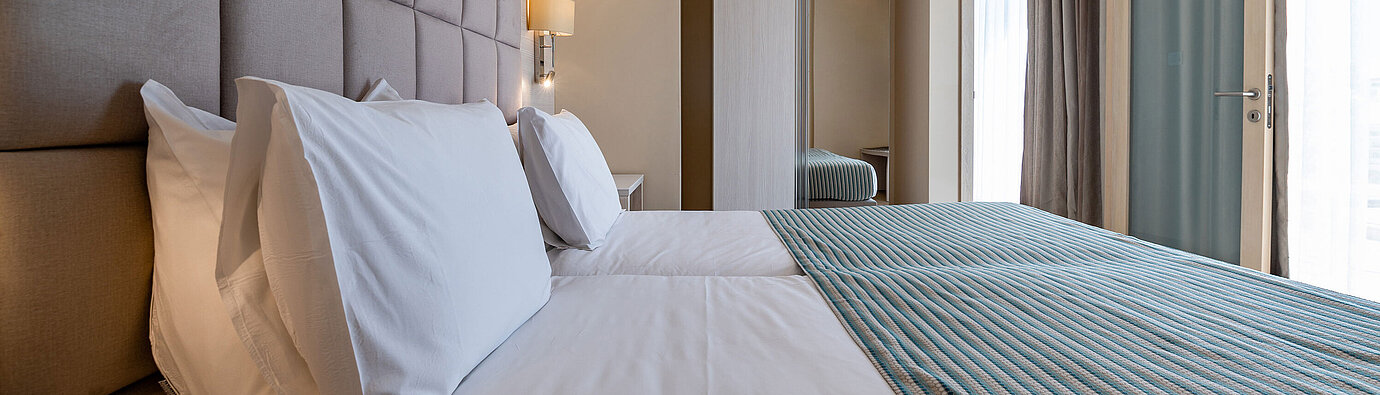 Stilvoller Schlafbereich der Junior Suite im Maritim Antonine Hotel & Spa Malta mit komfortablem Doppelbett, gepolstertem Kopfteil, modernem Kleiderschrank und bodentiefen Fenstern.