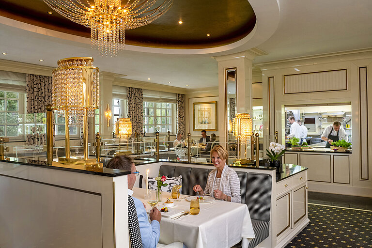 Paar genießt ein feines Dinner im luxuriösen Restaurant Orangerie des Maritim Timmendorfer Strand mit Blick in die Küche.