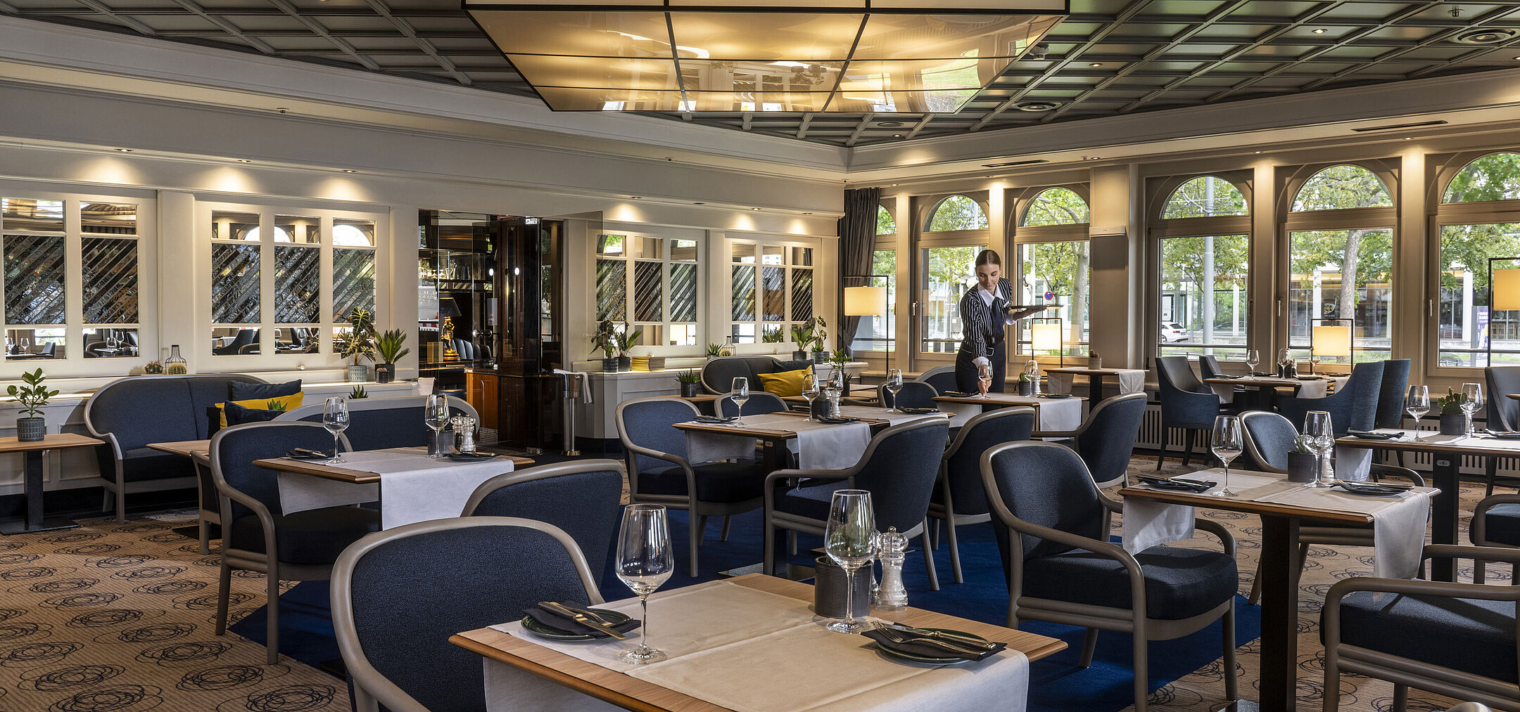 Modernes Restaurant im Maritim Darmstadt mit gedeckten Tischen und elegantem Design. Eine Mitarbeiterin sorgt für den Service