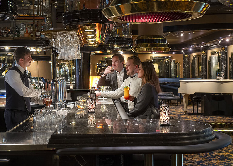 Gäste genießen Cocktails an der Pianobar im Maritim Hotel Köln, während der Barkeeper sie bedient.