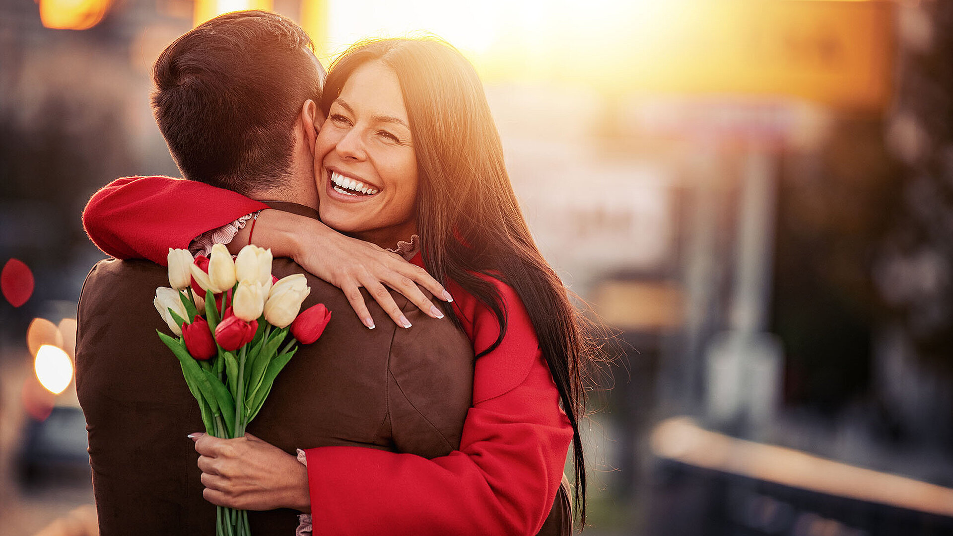Glückliches Paar umarmt sich bei Sonnenuntergang in der Stadt mit Blumenstrauß