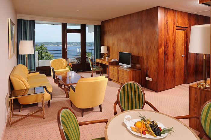 Junior Suite im Maritim Hotel Kiel, gemütliche Sitzecke, Schreibtisch, TV und Balkon mit Blick auf das Wasser.