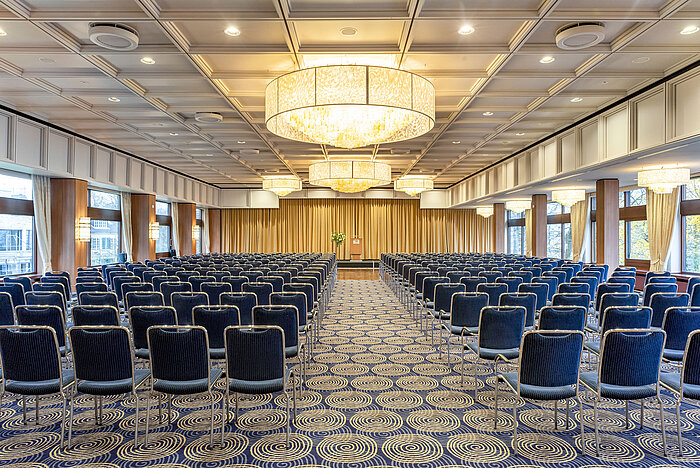 Saal Maritim im Maritim Hotel Kiel, großer Konferenzraum mit Reihenbestuhlung, Kronleuchtern und Bühne vor einem Vorhang.