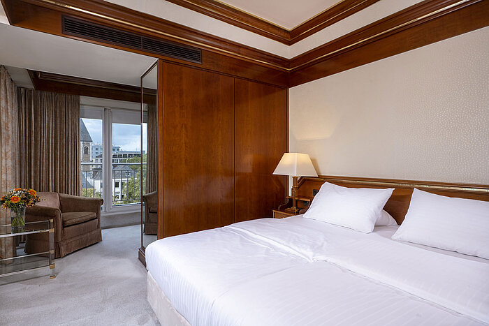 Helles Schlafzimmer in der Heumarkt-Suite des Maritim Köln mit gemütlichem Doppelbett, Holzdetails und Zugang zum Balkon.