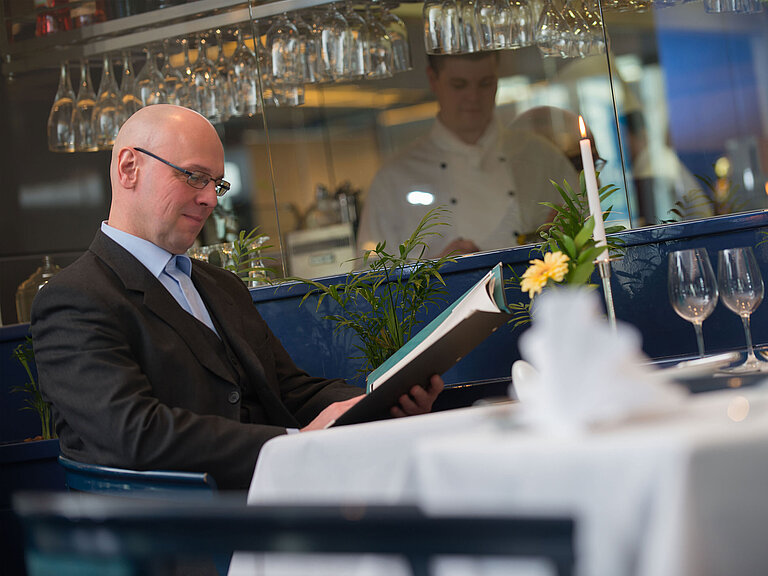 Eleganter gedeckter Tisch im Restaurant des Maritim Hotel Magdeburg mit einem Gast beim Studieren der Speisekarte.