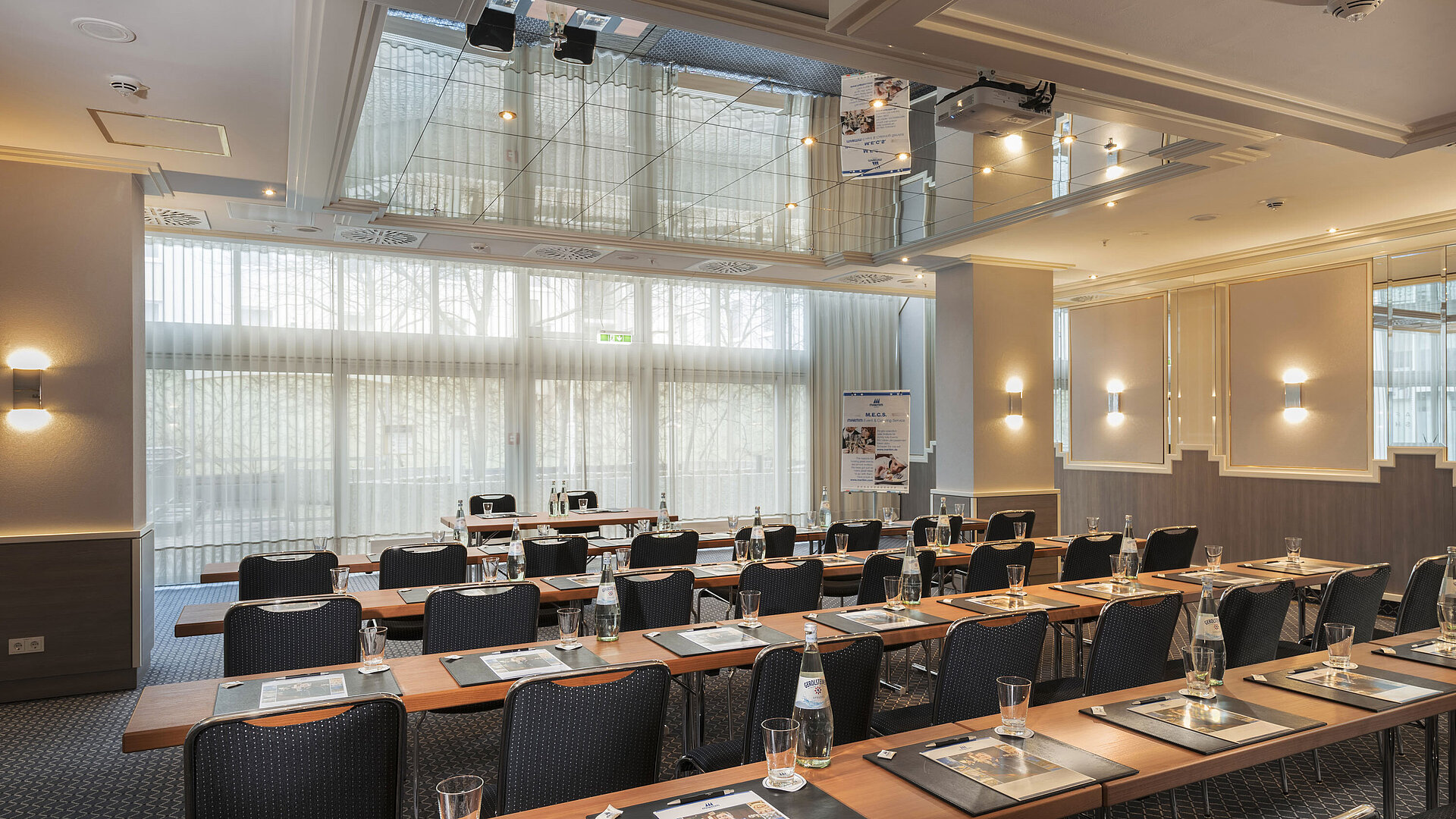 Tagungsraum mit Fensterfront, Tischen und Wasserflaschen im Maritim Hotel München