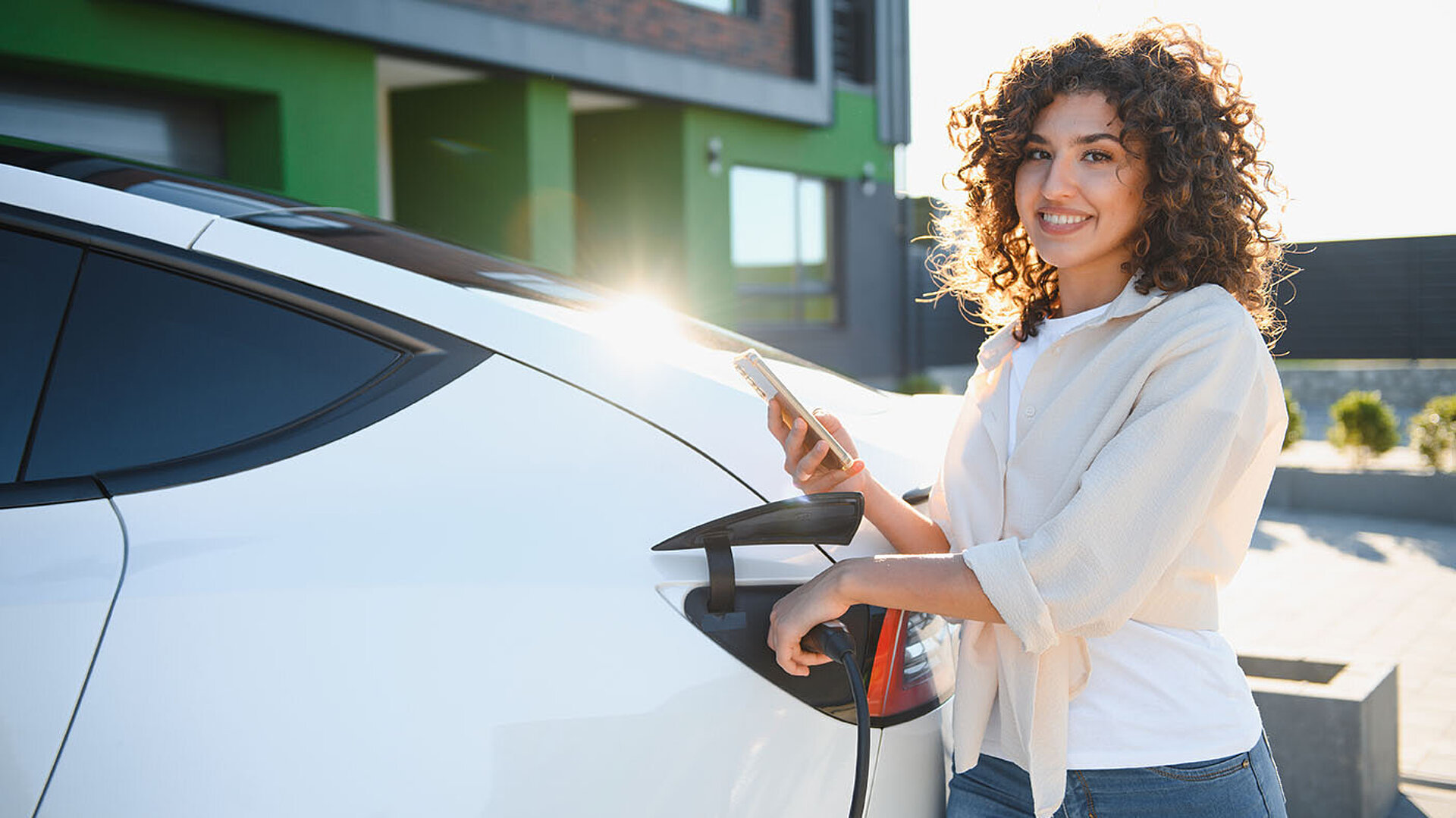 Frau lädt ein Elektroauto an einer Ladestation vor einem Hotel.