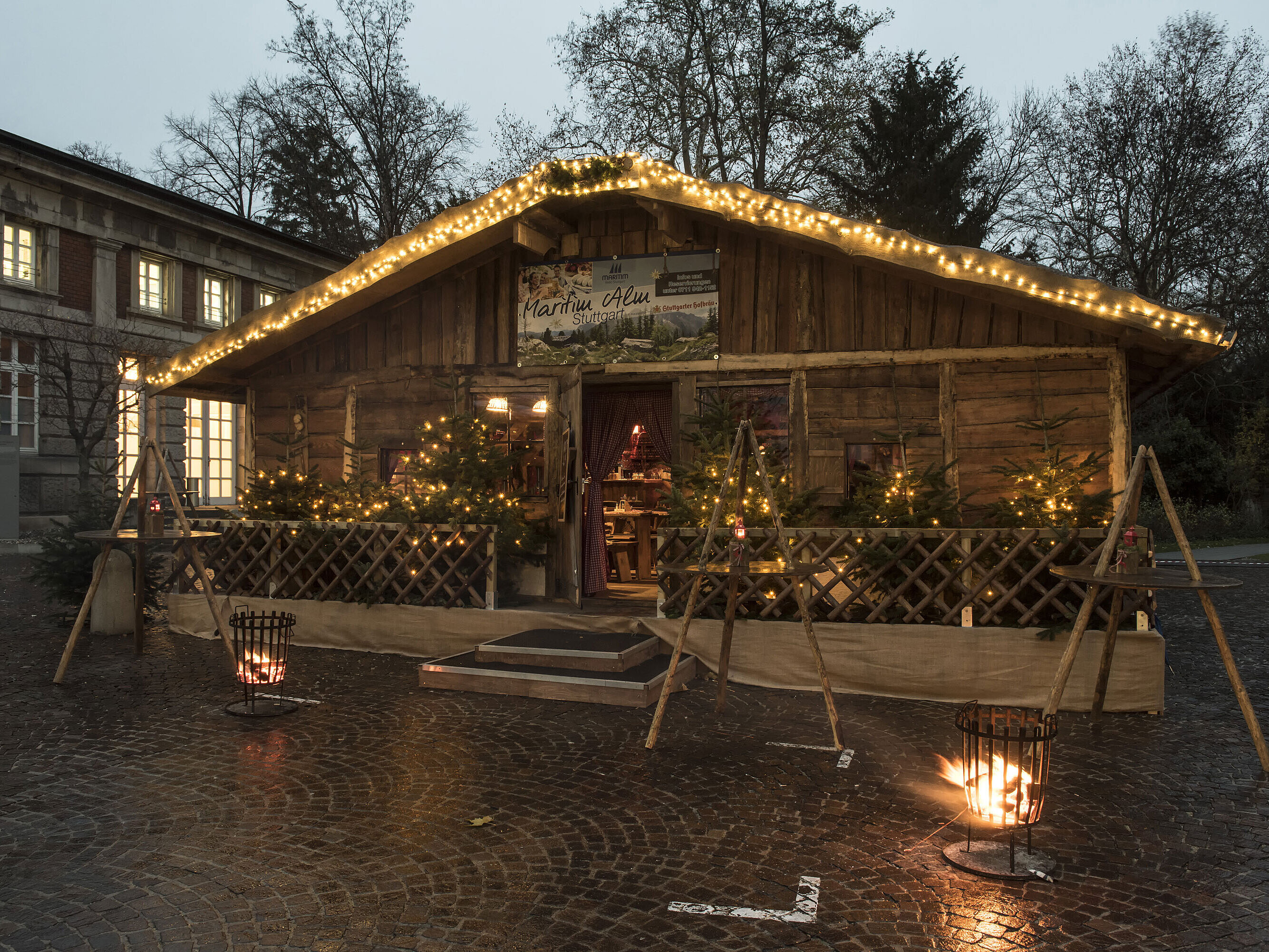Maritim Alm Stuttgart bei Dämmerung mit Weihnachtsbeleuchtung, Tannen und Feuerkörben vor dem Maritim Hotel