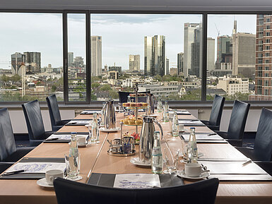 Tagungsraum im Maritim Hotel Frankfurt mit Blick auf die Skyline. Eleganter Tisch, Getränke und Snacks für Meetings bereitgestellt.