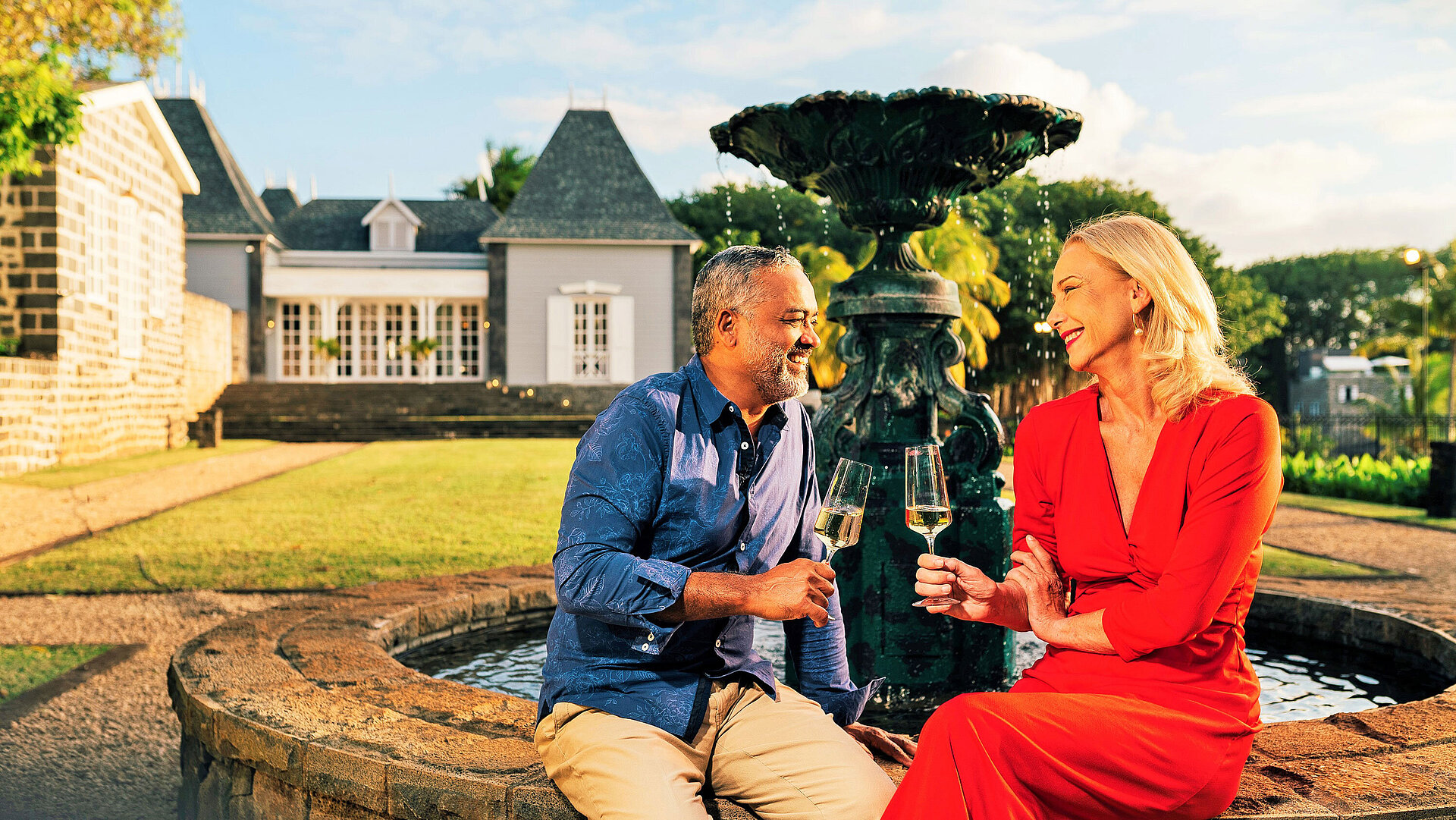 Paar genießt ein Glas Wein am Brunnen im gepflegten Garten bei Abendstimmung
