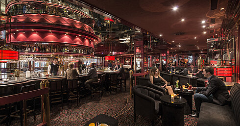 Gäste genießen Drinks in der atmosphärisch beleuchteten roten Hotelbar im Maritim Hotel Stuttgart
