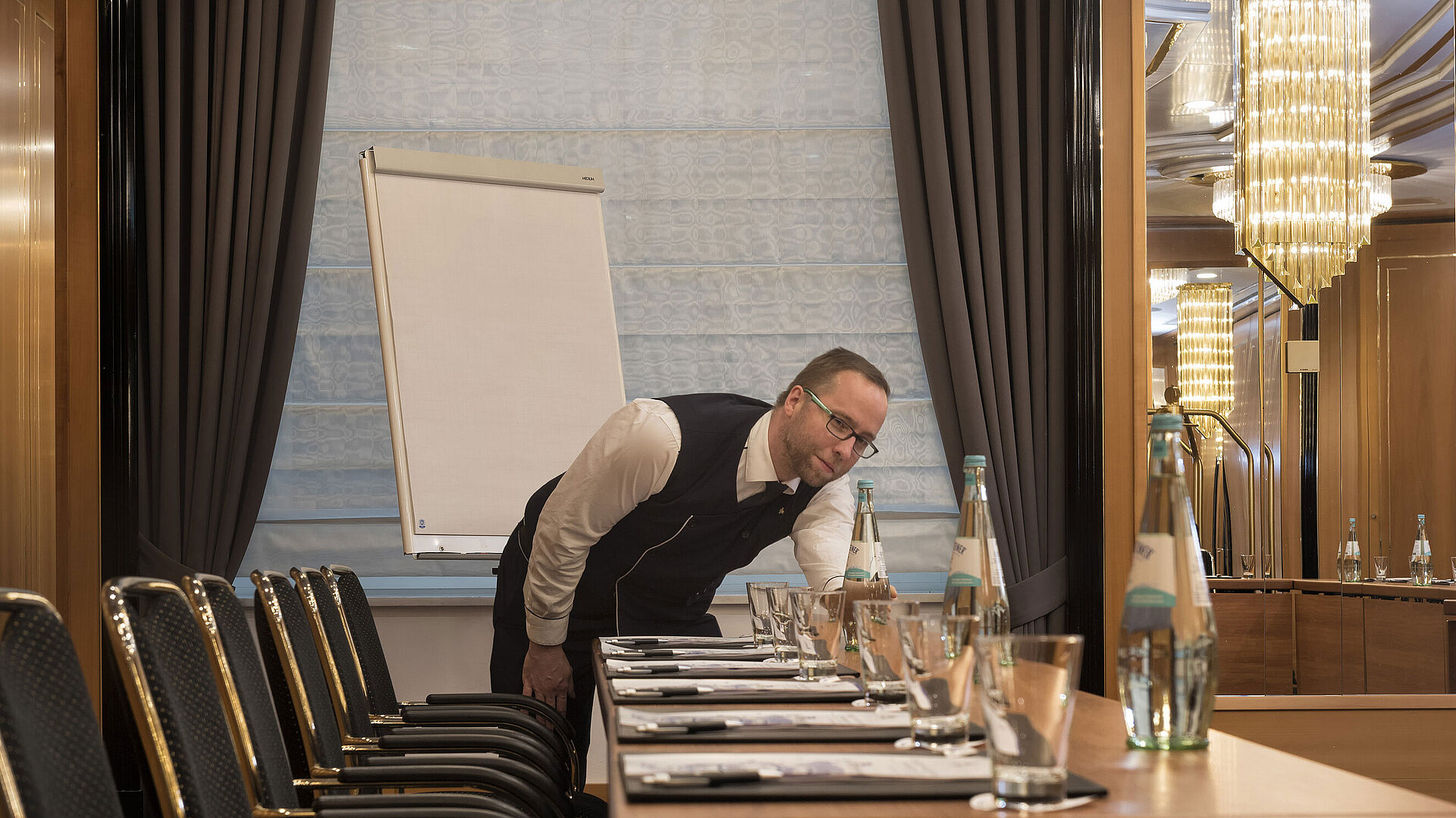 Mitarbeiter bereitet Konferenztisch mit Wasserflaschen und Gläsern im Maritim Hotel Stuttgart vor