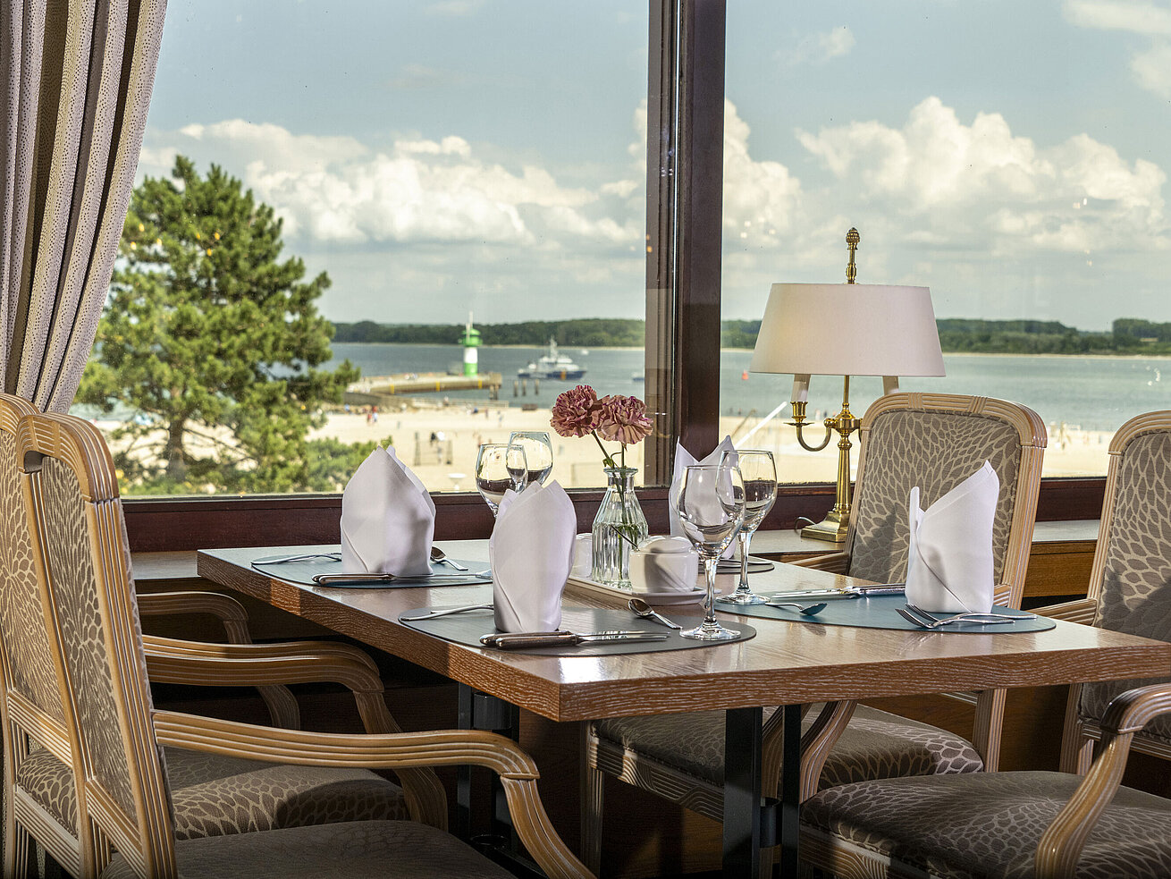 Gedeckter Tisch am Fenster mit Ausblick auf den Strand und Leuchtturm im Maritim Hotel Travemünde