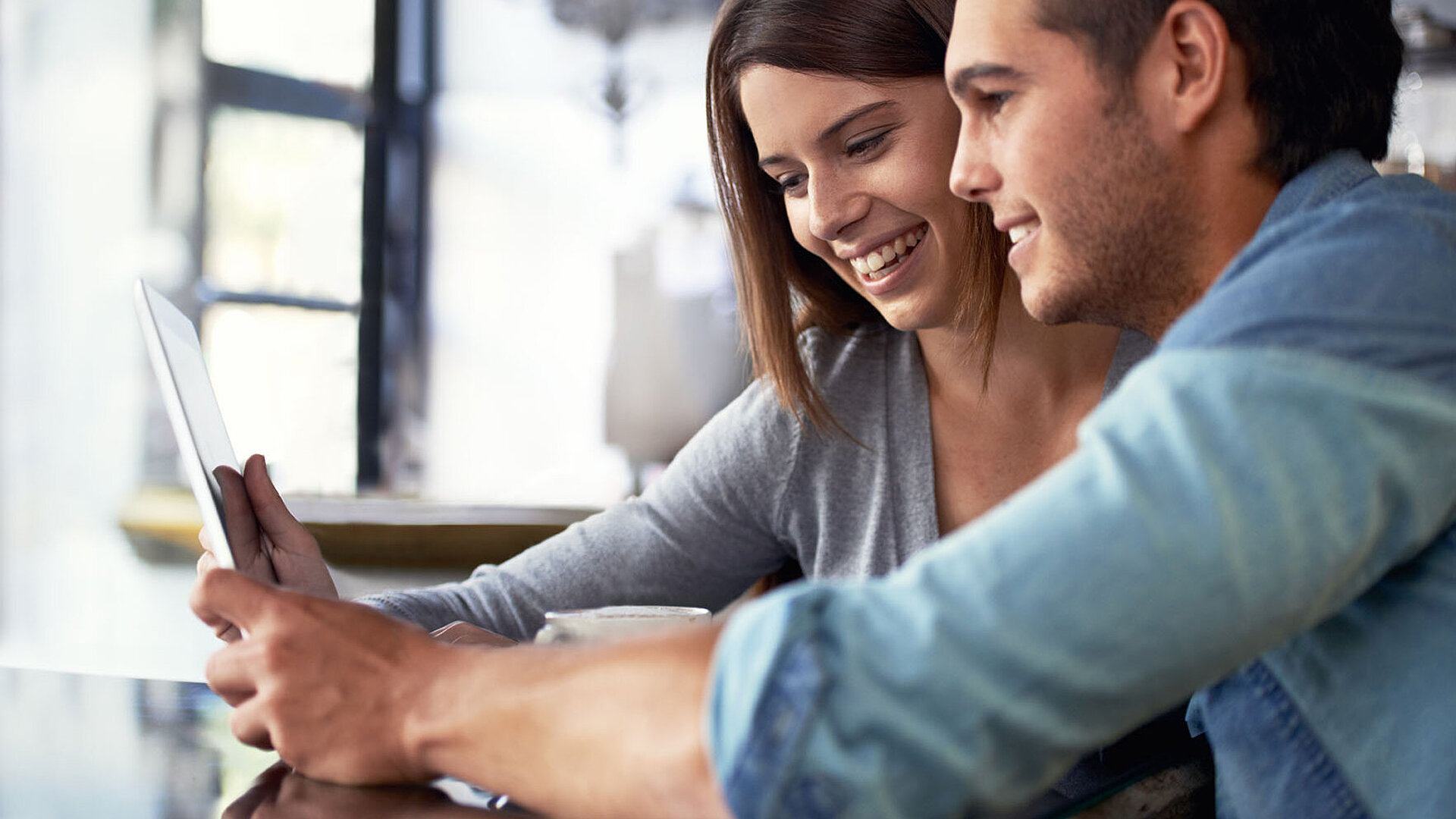 Junges Paar sitzt im Café und schaut gemeinsam auf ein Tablet