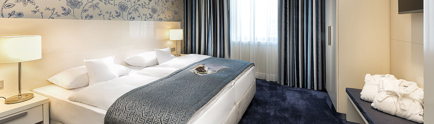 Elegante Suite im Maritim Hotel Bonn mit einem großen Bett, blauer Bettdecke und stilvollem Dekor.