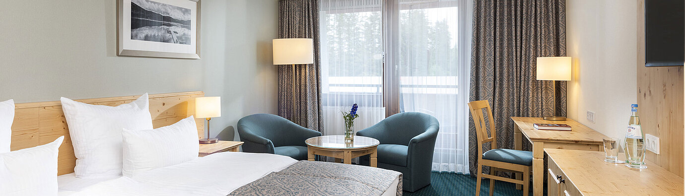 Helles Doppelzimmer im Maritim TitiseeHotel mit Sitzbereich, Schreibtisch und Blick auf den Wald