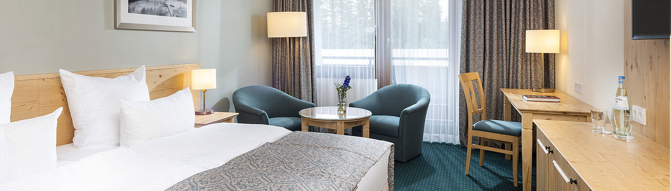 Helles Doppelzimmer im Maritim TitiseeHotel mit Sitzbereich, Schreibtisch und Blick auf den Wald