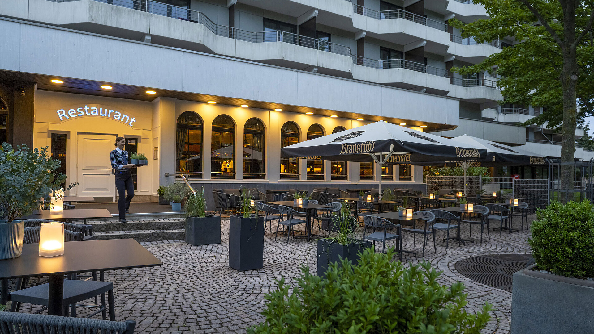 Abendstimmung auf der Terrasse des Maritim Hotels Darmstadt mit einem Mitarbeiter, der ein Tablett zum Restaurant trägt.