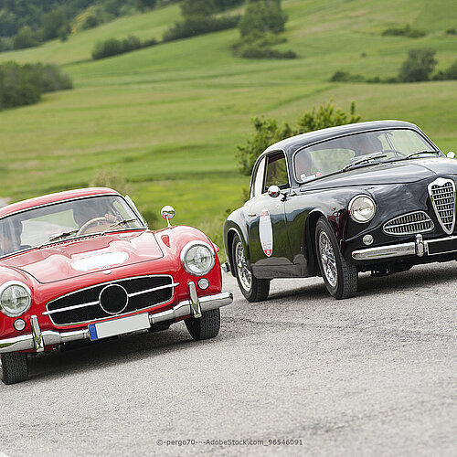 Zwei klassische Oldtimer fahren auf einer Landstraße durch grüne Hügellandschaft bei einer Ausfahrt