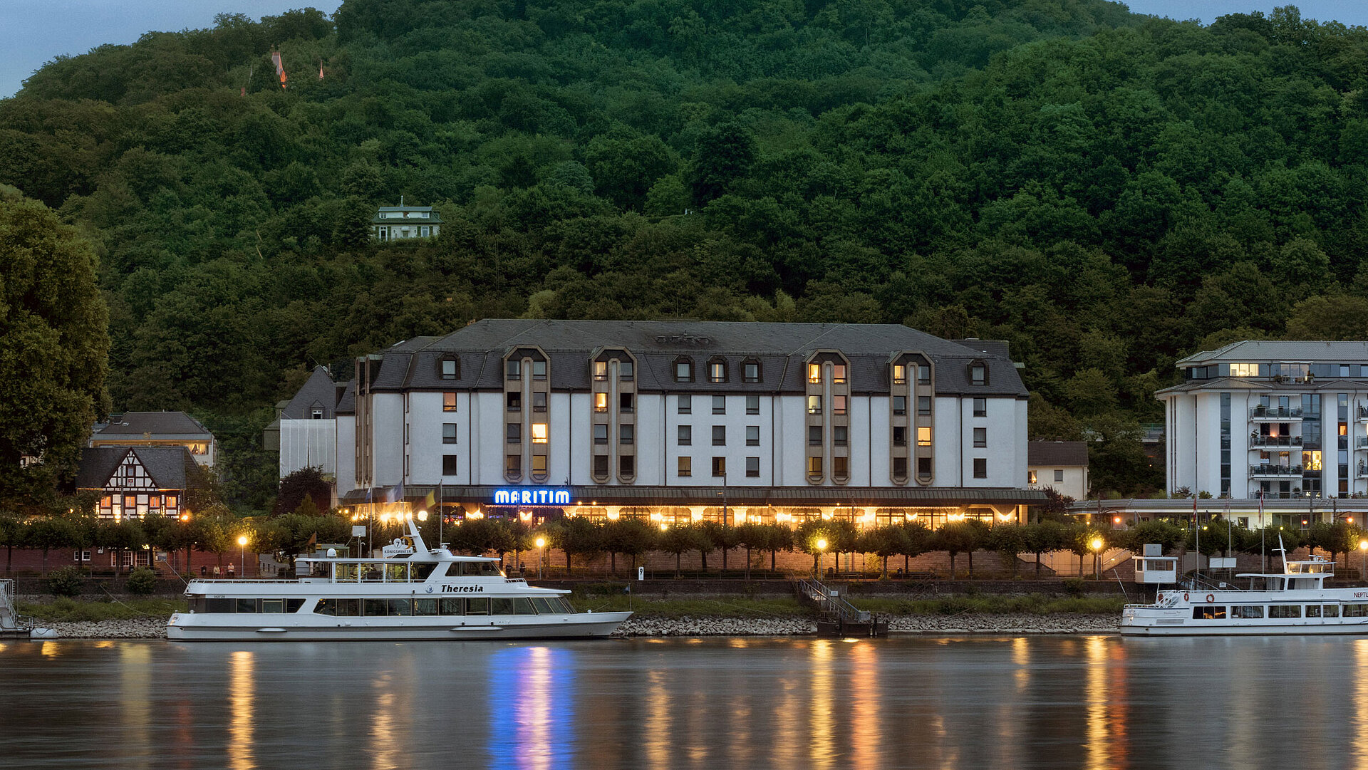 Das Maritim Hotel Königswinter bei Nacht mit stimmungsvoller Beleuchtung und Blick auf den Rhein.
