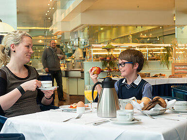 Eine Mutter und ihr Sohn genießen ein entspanntes Frühstück im Maritim Hotel Magdeburg,mit Blick auf das Buffet im Hintergrund