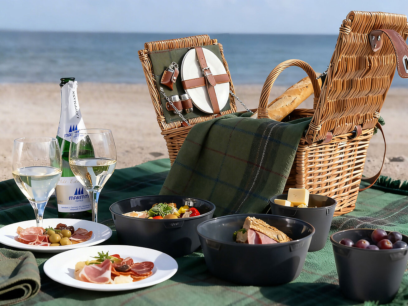 Picknickkorb mit Snacks, Obst und Getränken am Strand mit Blick auf das Meer.