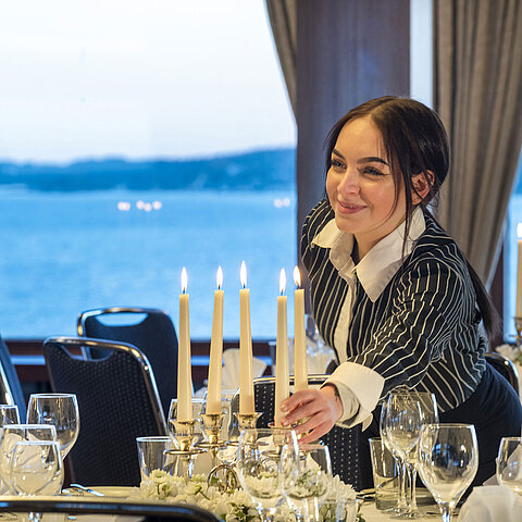 Saal Maritim im Maritim Hotel Kiel, eine Mitarbeiterin zündet Kerzen auf einem festlich gedeckten Tisch an, im Hintergrund Meerblick.