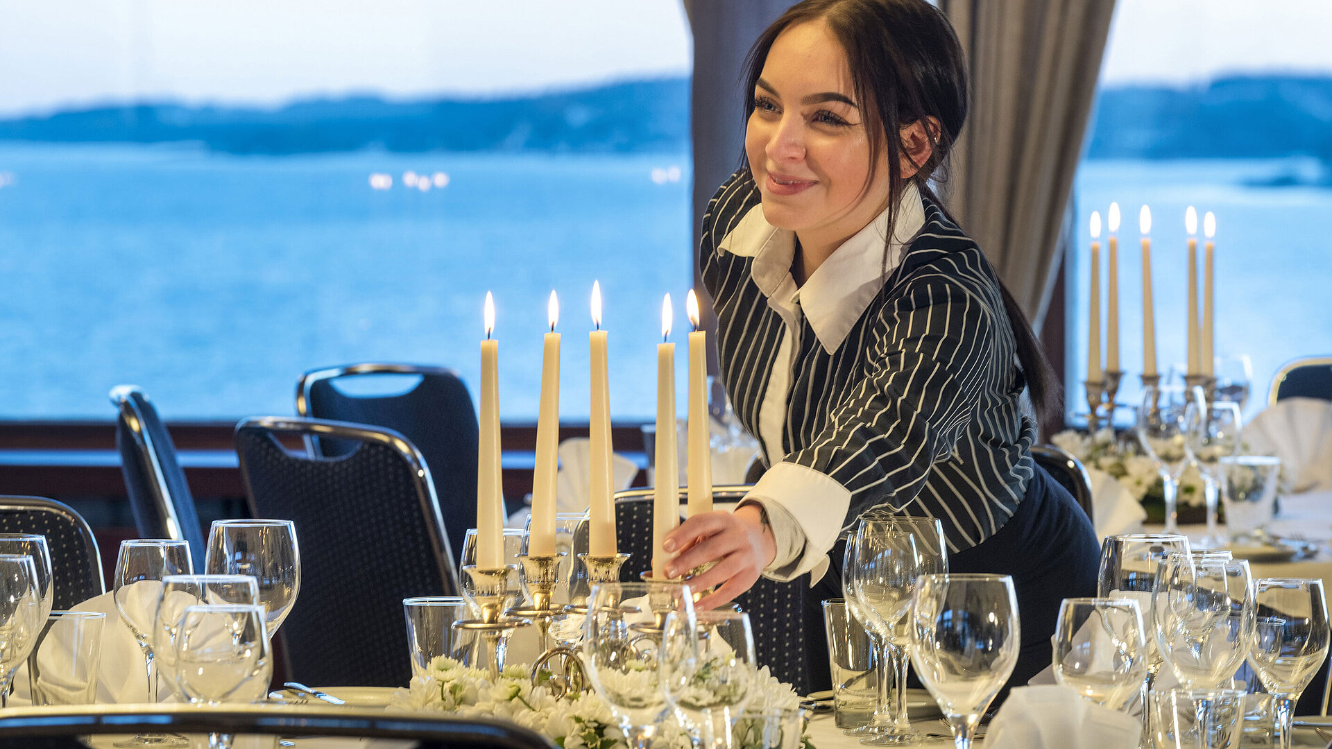 Saal Maritim im Maritim Hotel Kiel, eine Mitarbeiterin zündet Kerzen auf einem festlich gedeckten Tisch an, im Hintergrund Meerblick.