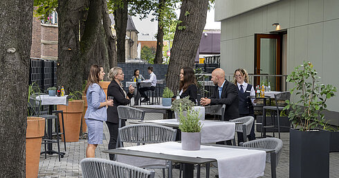 Moderne Terrasse im Maritim Hotel Darmstadt mit Gästen, die entspannen, Bäumen im Hintergrund und stilvollen grauen Möbeln.
