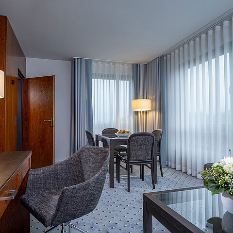 Elegantes Suite-Wohnzimmer im Maritim Bremen mit gemütlicher Sitzecke, Schreibtisch, TV und frischen Blumen als Dekoration.