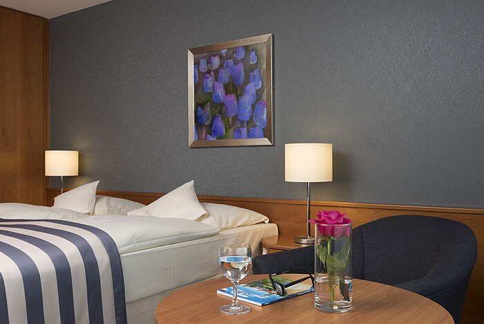 Detail im Maritim Hotel Ulm: Tisch mit Rose, Wasser, Brille und Reisebroschüre vor Doppelbett