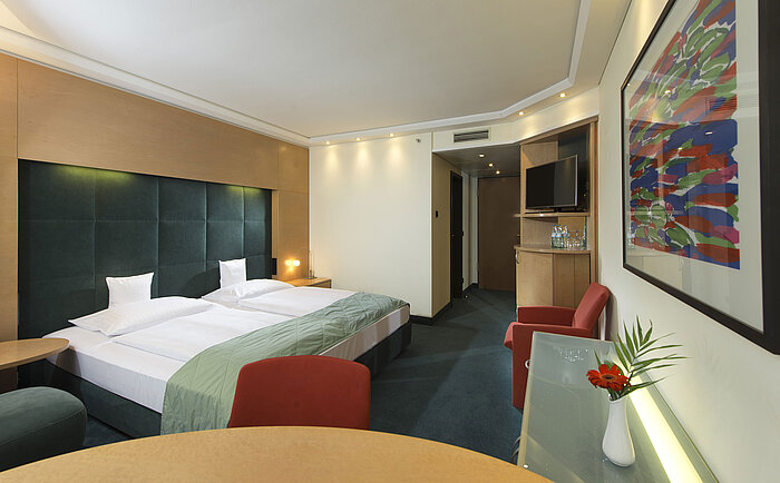 Komfort-Zimmer im Maritim proArte Hotel Berlin, ausgestattet mit modernen Möbeln, Doppelbett, Kunstwerk und Schreibtisch.