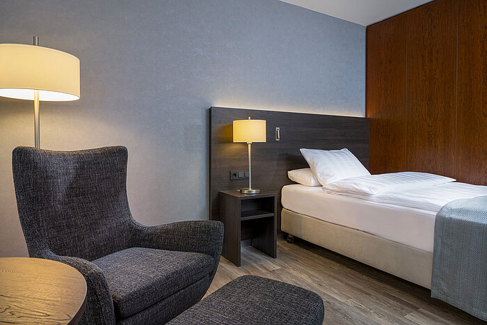 Modernes Superior Queen Zimmer im Maritim Hotel Bremen mit gemütlichem Sessel, Nachttisch und stimmungsvoller Beleuchtung.