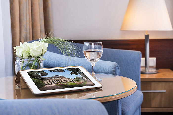 Gemütlicher Sitzbereich im Maritim Hotel Fulda mit Tablet, Glas Wasser und weißen Rosen auf einem Glastisch.