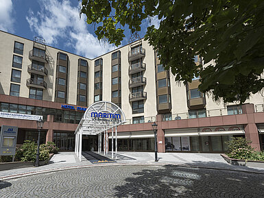 Eingangsbereich des Maritim Hotel Bad Homburg mit moderner Glasüberdachung und grüner Umgebung.