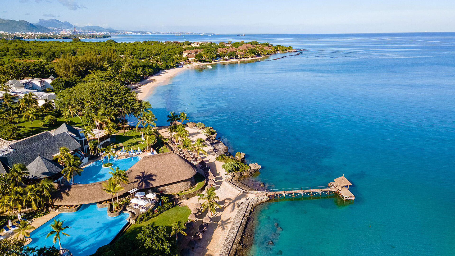 Luftaufnahme eines Strandresorts mit Pool, Palmen und direktem Zugang zum türkisblauen Meer