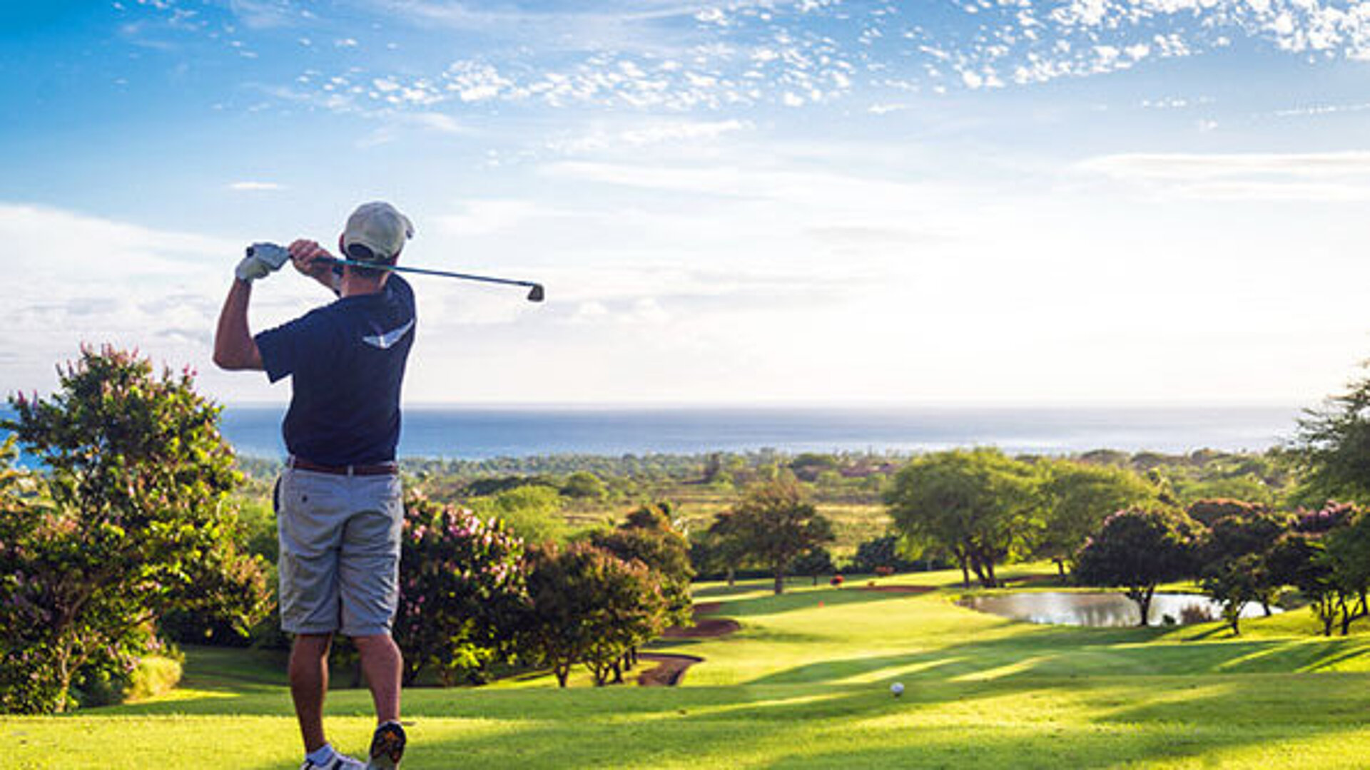 Golfer beim Abschlag auf einem sonnigen Golfplatz mit Blick über das gepflegte Fairway und die Landschaft.