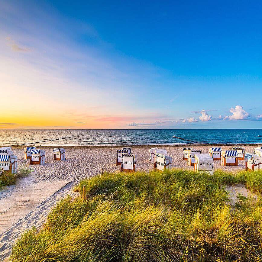 Strand mit Strandkörben und Dünen an der Ostsee bei Sonnenuntergang