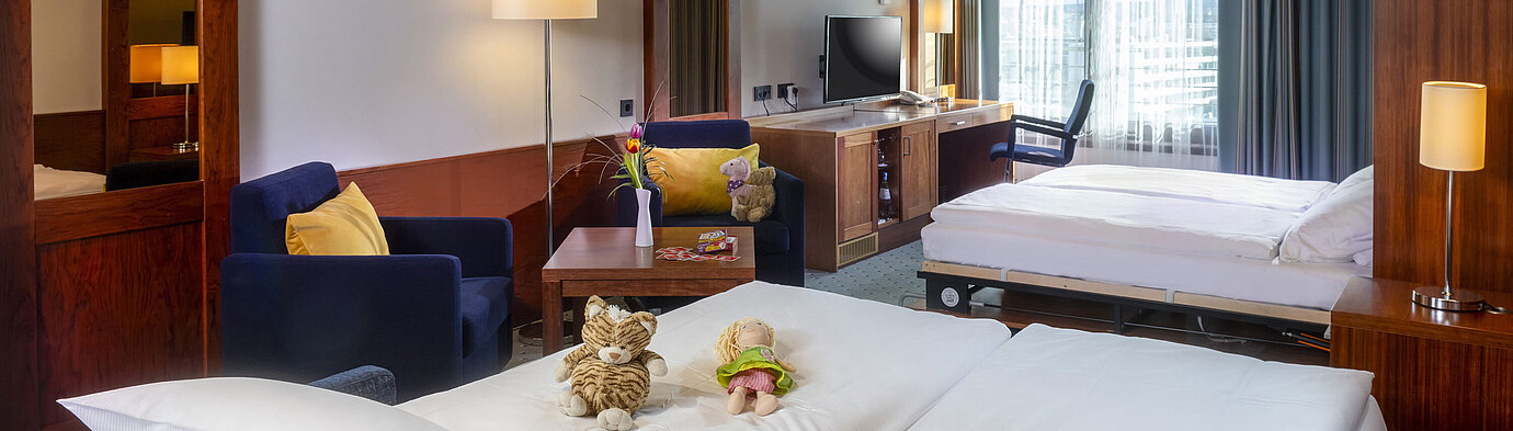 Familienzimmer im Maritim Hotel Darmstadt mit Spielzeug auf dem Bett,einem Schreibtisch mit TV und einer gemütlichen Sitzecke
