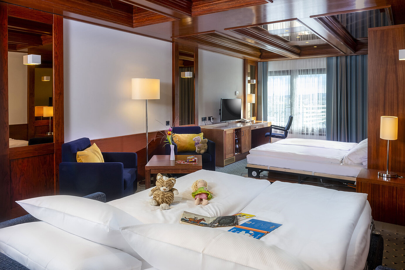 Familienzimmer im Maritim Hotel Darmstadt mit Spielzeug auf dem Bett,einem Schreibtisch mit TV und einer gemütlichen Sitzecke