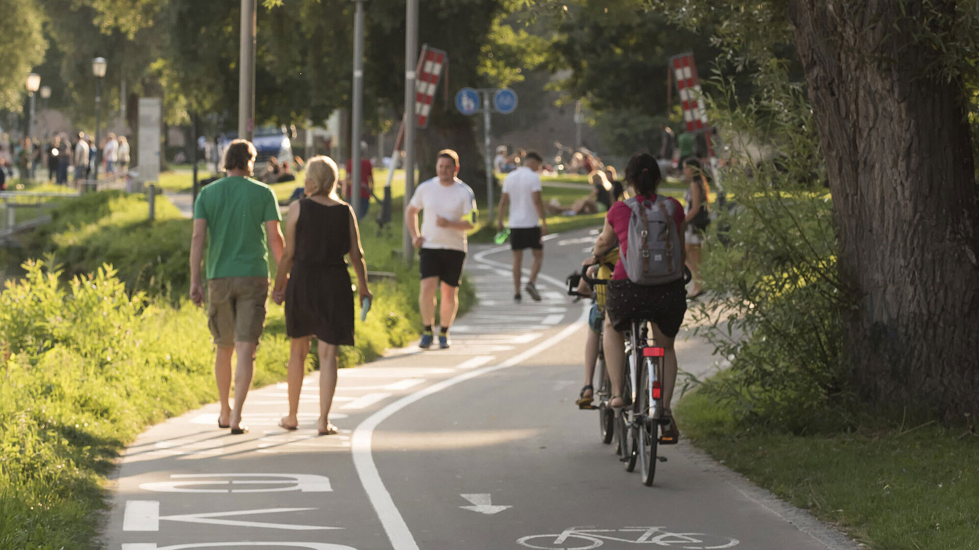 Fußgänger und Radfahrer an der Donaupromenade in Ulm bei Sonnenschein.
