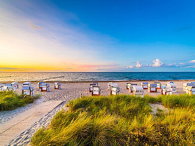 Strand mit Strandkörben und Dünen an der Ostsee bei Sonnenuntergang