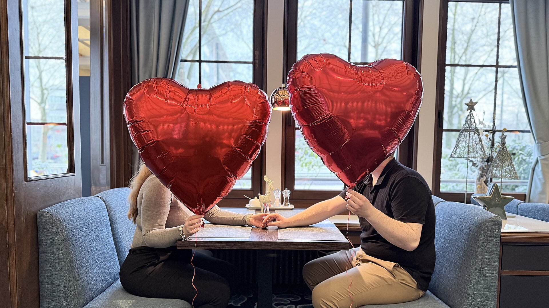 Paar sitzt sich gegenüber im Restaurant mit Herzballons und genießt einen romantischen Valentinstag.