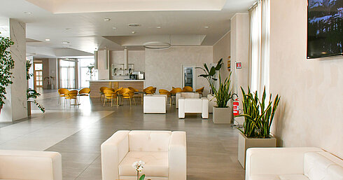 Lichtdurchflutete Lobby des Maritim Resort Calabria mit weißen Sesseln und gelben Stühlen
